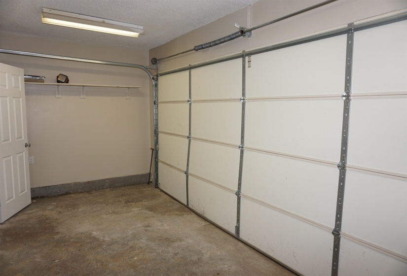 Garage space featuring a paneled overhead door, concrete flooring, fluorescent ceiling light fixture, and a built-in wall shelf
