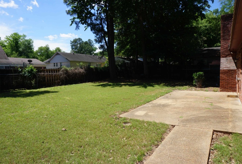 Spacious backyard featuring a manicured lawn, established shade trees, and a concrete patio