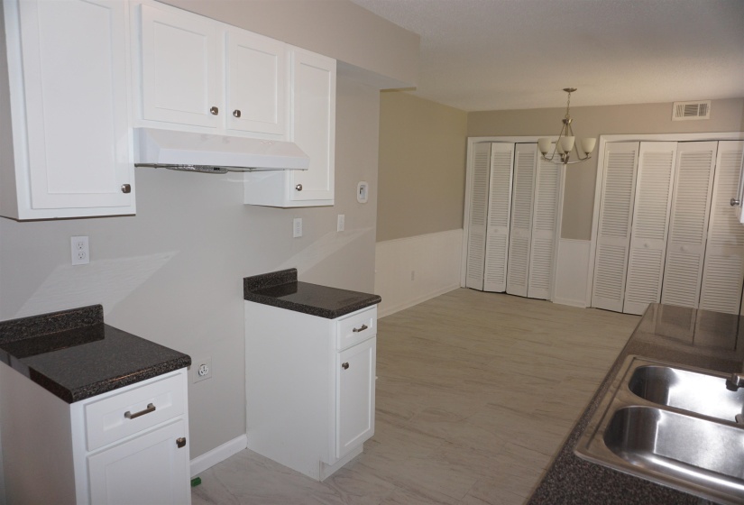Kitchen and dining area featuring white cabinetry, dark speckled countertops, a double-basin stainless steel sink, and wood-finish flooring
