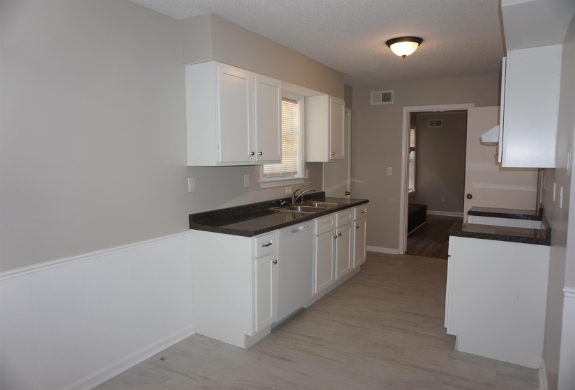 Kitchen featuring white cabinetry, dark countertops, a double basin sink, and light wood-finish flooring