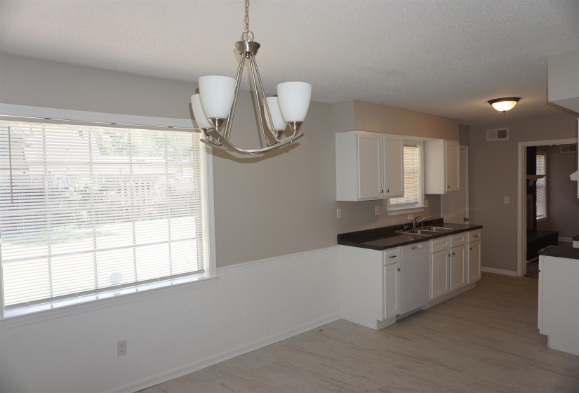 Open-concept kitchen and dining area featuring a modern chandelier, light wood-finish flooring, white cabinetry, dark countertops, and a double-basin sink