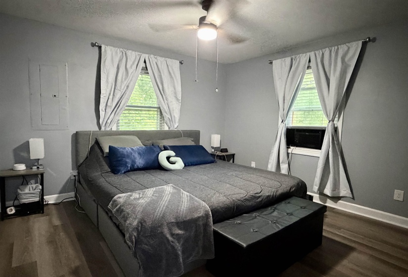 Room featuring wood-finish flooring, two windows with window treatments, a ceiling fan with integrated lighting, and neutral wall paint