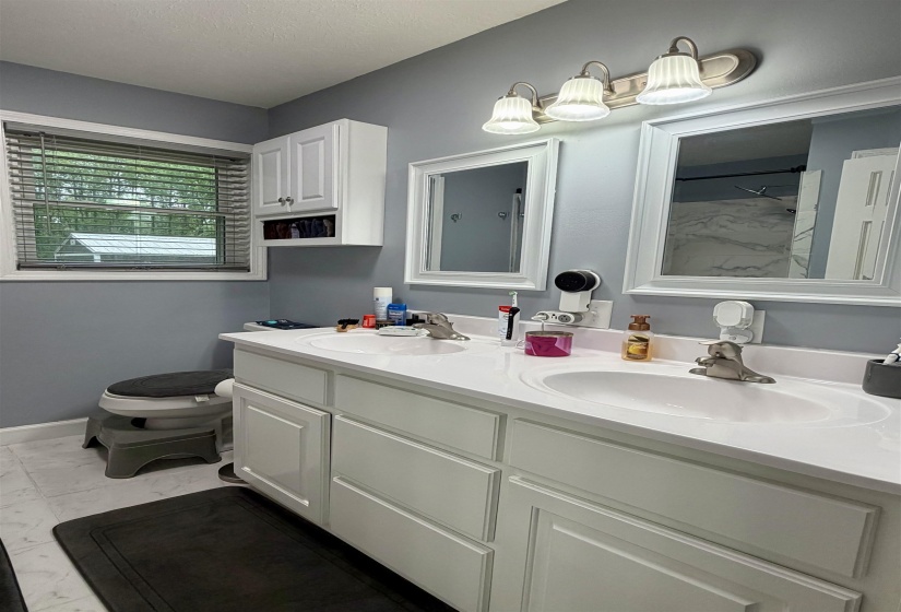 Double vanity with white cabinetry, integrated sinks, chrome-finish fixtures, and a coordinating overhead light fixture