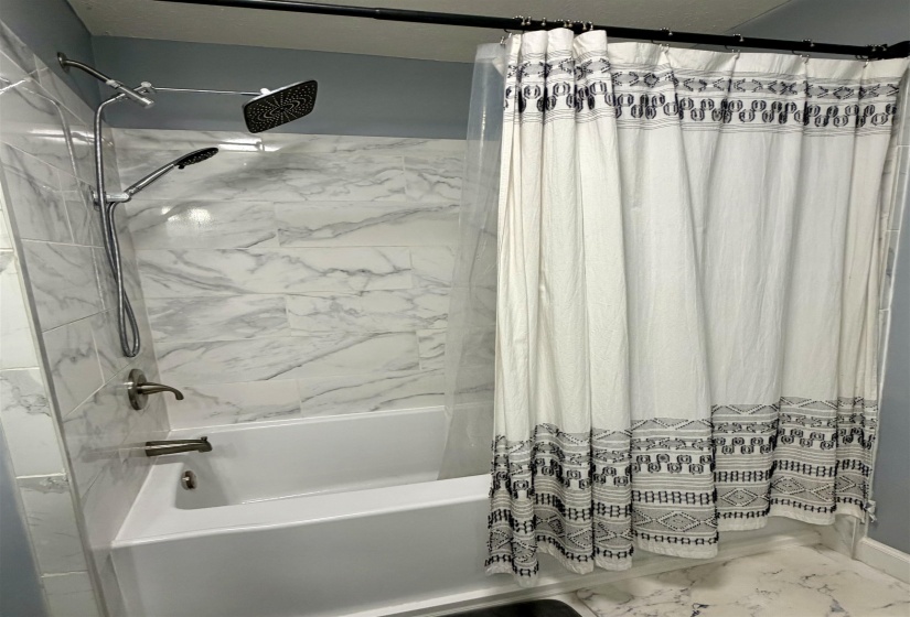 Bathtub with marble-look tiled surround, dual shower heads, and brushed nickel fixtures