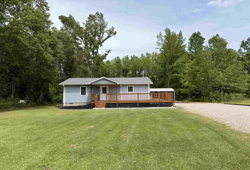 Light blue siding exterior featuring a covered porch with natural wood railings, a gravel driveway, and a spacious green lawn