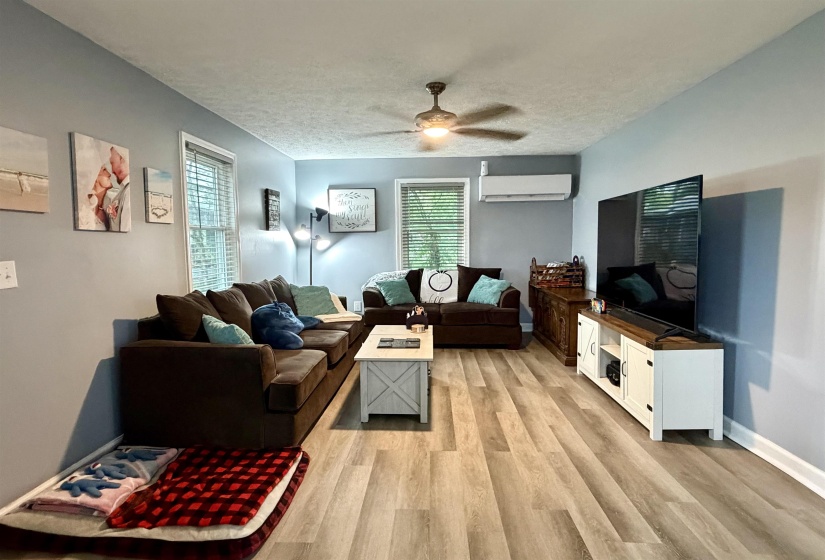 Spacious living area featuring wood-finish flooring, a ceiling fan, and window blinds