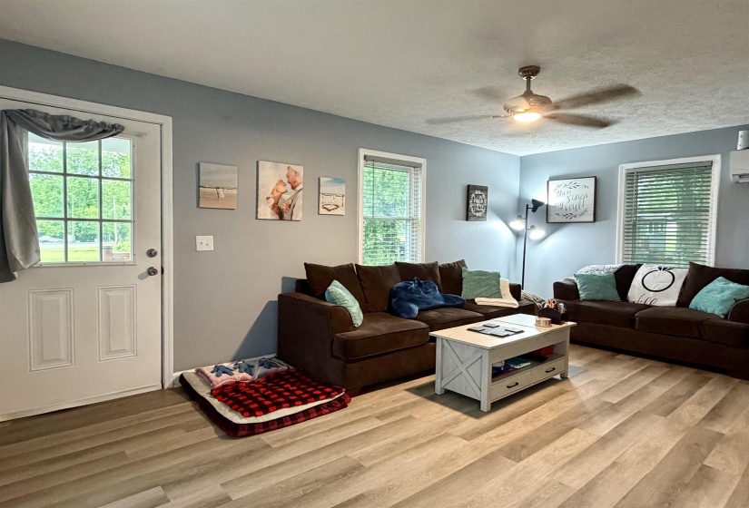 Living area featuring wood-finish flooring, light blue wall paint, and multiple windows with blinds