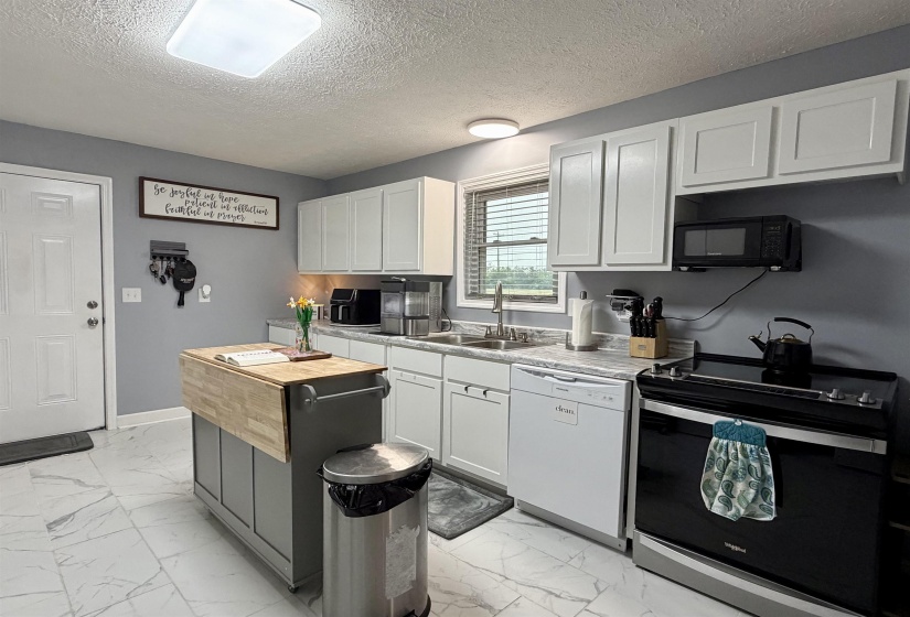 Kitchen featuring white cabinetry with brushed nickel hardware, light-toned countertops, stainless steel sink, black and stainless steel range, and marbling-patterned flooring