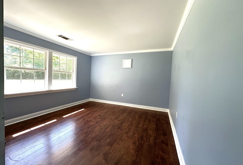 Spacious room featuring two large windows, wood-finish flooring, light blue walls, and white crown molding
