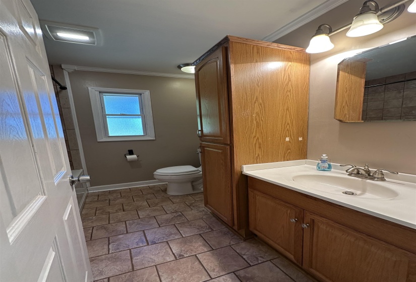 Bathroom featuring a vanity with an integrated sink, wood-finish cabinetry, a tall storage cabinet, tiled flooring, and a window for natural light