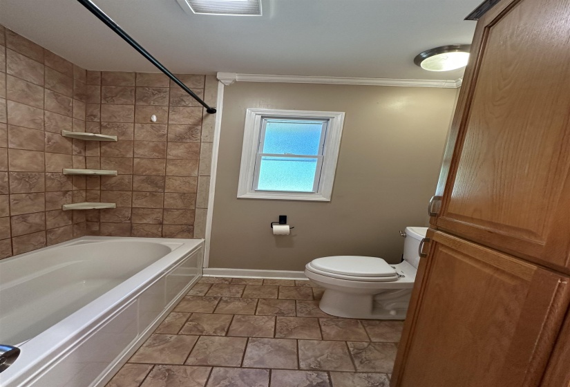 Full bathroom featuring a tiled tub surround with built-in shelving, a single window, and a built-in wood-finish cabinet