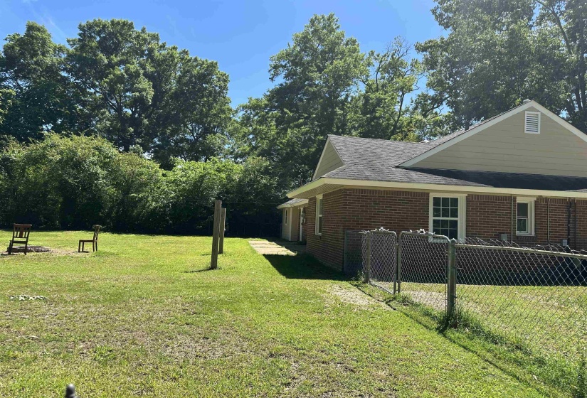 Expansive rear yard featuring mature perimeter trees, a lush green lawn, and a partial chain-link fence