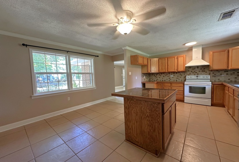 Kitchen area with a built-in island featuring a dark countertop, wood-finish cabinetry, a tiled backsplash, a white range with a matching range hood, and tile flooring