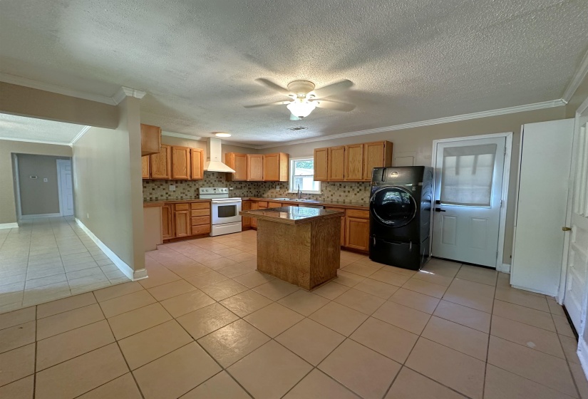 Spacious kitchen featuring tile flooring, wood cabinetry, stone countertops, a tiled backsplash, and a central island
