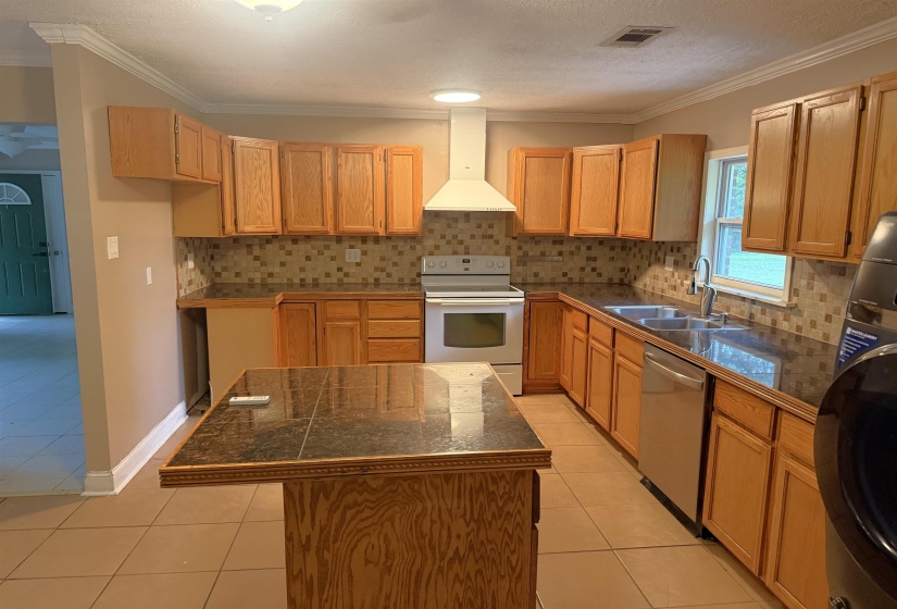 Kitchen featuring wood cabinetry, dark countertops, a mosaic tile backsplash, stainless steel appliances, and a central island with a matching countertop