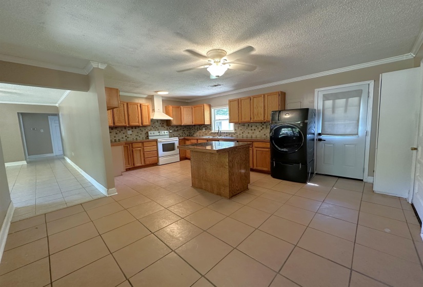 Kitchen featuring wood-finish cabinetry, a central island with a stone-finish countertop, patterned tile backsplash, and tile flooring