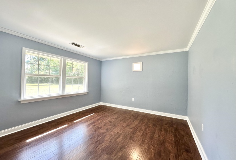Bright interior space featuring wood-finish flooring, two large windows, light blue painted walls, white crown molding, and white baseboards