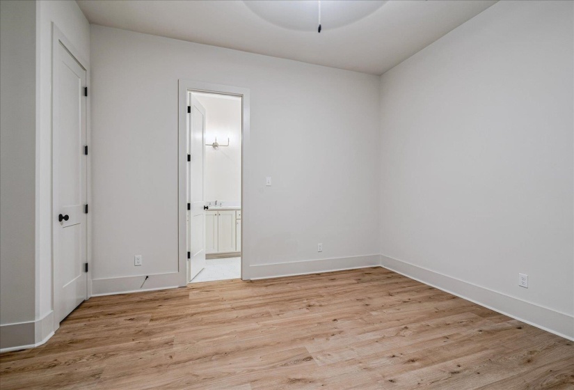Spacious interior room featuring wood-finish flooring, white baseboards, and a white door with black hardware