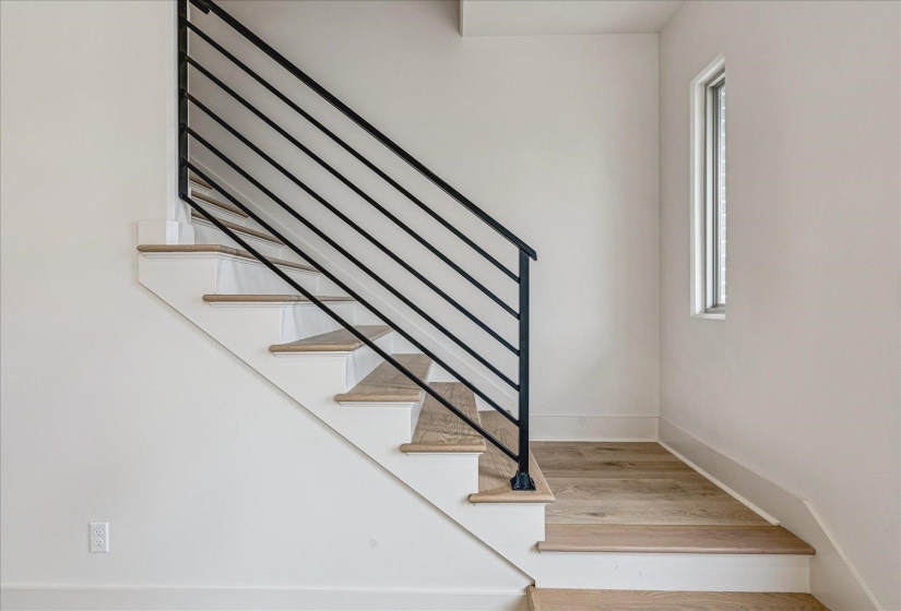 Modern staircase featuring a black metal horizontal baluster railing, white risers, and wood-finish treads