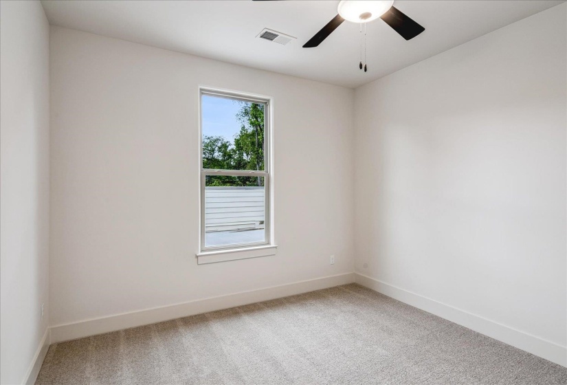 Bright room featuring a single window, light gray carpeting, and a ceiling fan with integrated lighting