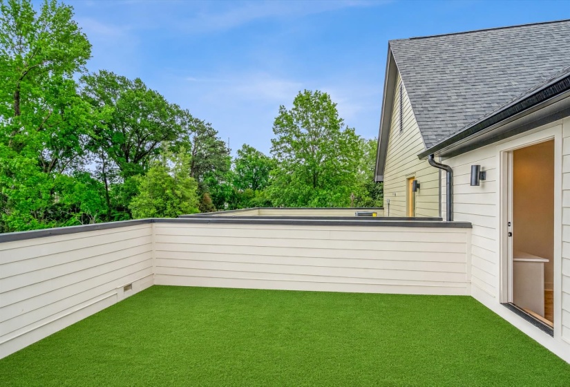 Outdoor terrace with artificial turf flooring, enclosed by white horizontal siding, featuring a doorway leading indoors