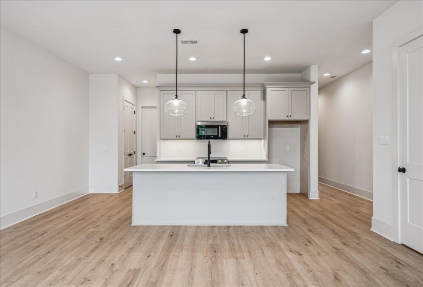 Open concept kitchen featuring light gray cabinetry, stainless steel appliances, and an island with an integrated sink