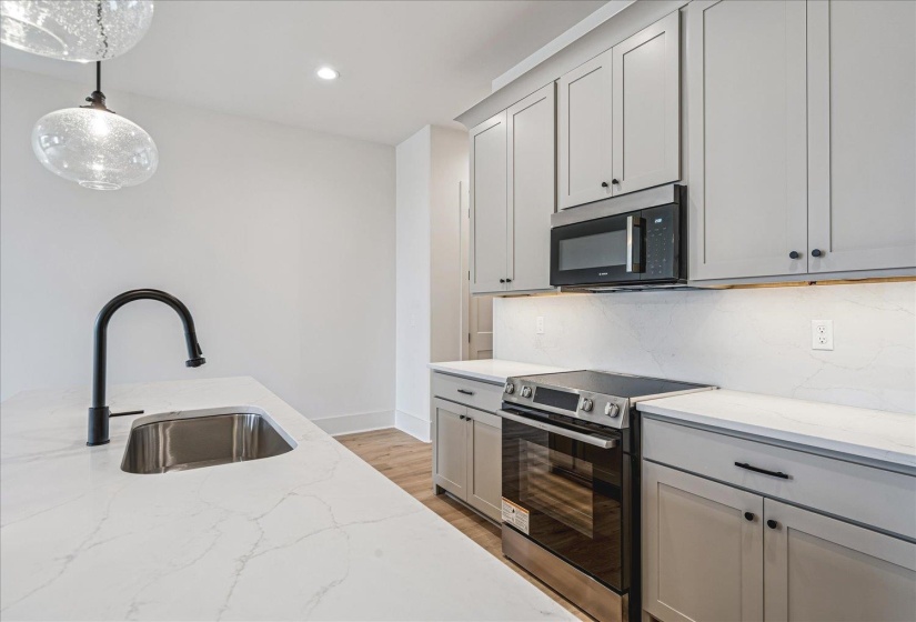 Kitchen featuring expansive white countertops, stainless steel sink with a matte black faucet, light gray cabinetry, and stainless steel appliances including a microwave and range