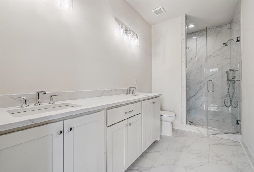 Bathroom featuring a dual vanity with white cabinetry, polished chrome fixtures, and a glass-enclosed shower with a handheld showerhead