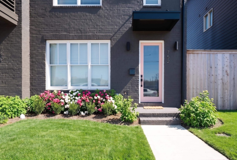 Contemporary facade with dark brick exterior, pink glass-paneled entry door, and a black awning