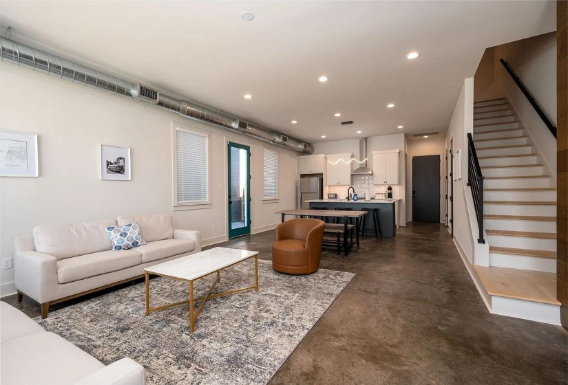 Open-concept living area featuring a kitchen island with seating, exposed spiral ductwork, wood-finish flooring on the staircase, and recessed lighting