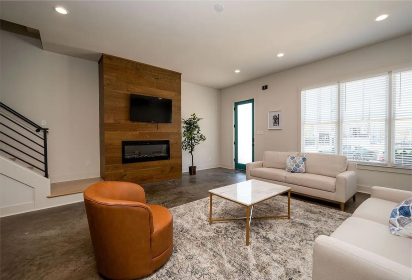 Living space featuring a wood-paneled accent wall with an integrated electric fireplace, multiple recessed lights, and large windows with blinds