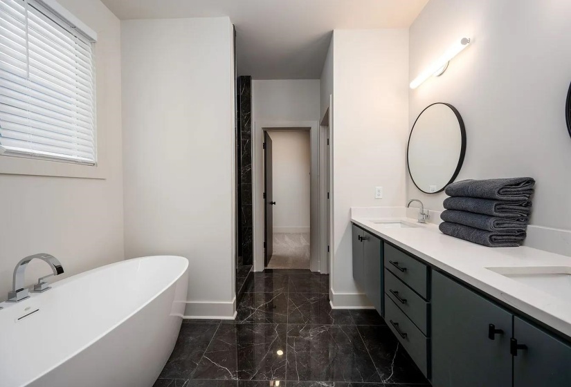 Bathroom featuring a freestanding soaking tub, dual vanity with undermount sinks, stone-look tile flooring, and a round wall-mounted mirror