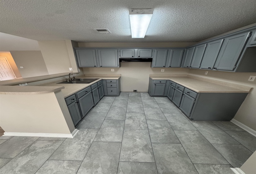 Kitchen with gray cabinetry, a peninsula, a textured ceiling, and light countertops