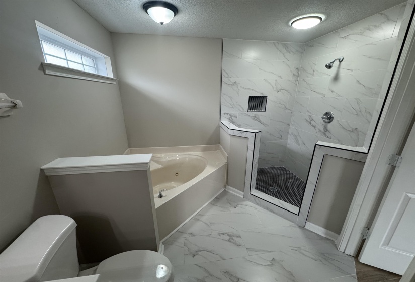 Bathroom featuring light marble finish floors, a textured ceiling, a marble finish shower, and a bath