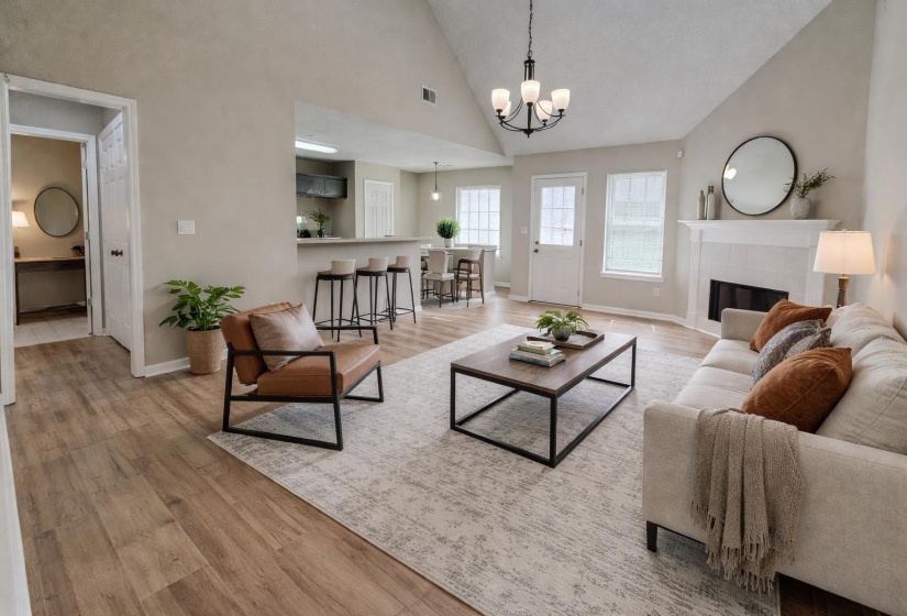 Living area with light wood finished floors, vaulted ceiling, a tiled fireplace, and suspended lighting