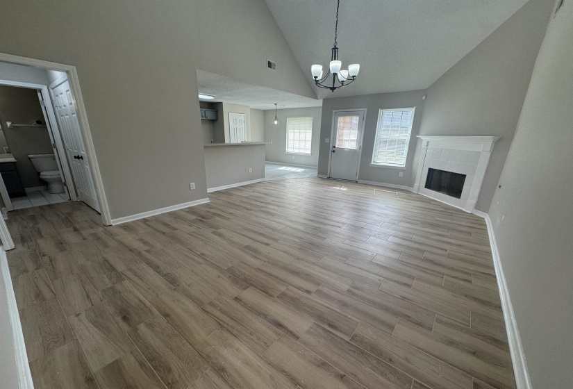 Unfurnished living room featuring vaulted ceiling, hanging lights, a tile fireplace, and light wood-style floors