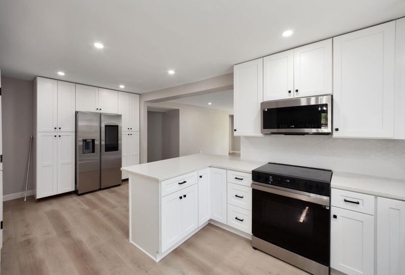 Modern kitchen featuring white shaker cabinetry, stainless steel appliances, light wood-finish flooring, recessed lighting, and a kitchen island with stone countertops