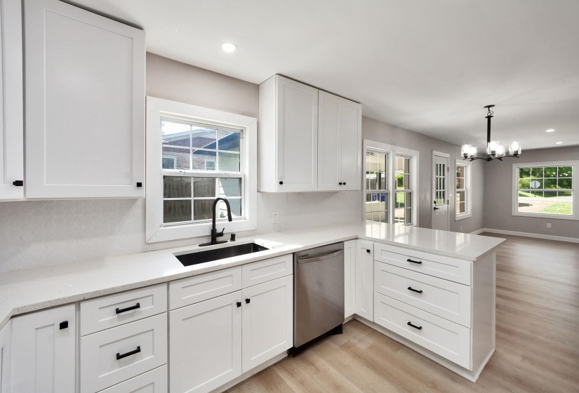 Kitchen featuring white shaker cabinetry, light-toned countertops, a matte black sink with matching faucet, and a stainless steel dishwasher
