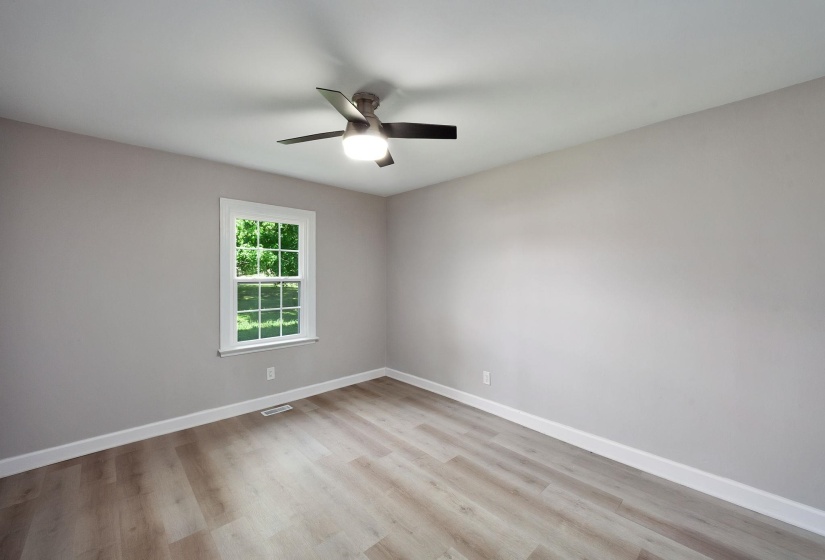 Interior room featuring light wood-finish flooring, a ceiling fan with integrated lighting, a double-hung window with a white frame, and light gray wall paint with white baseboards