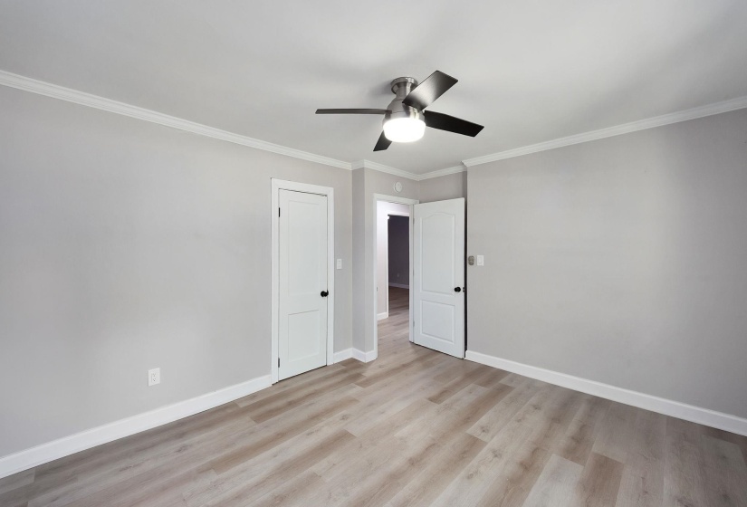 Spacious room featuring wood-finish flooring, white baseboards, crown molding, and a modern ceiling fan with lighting