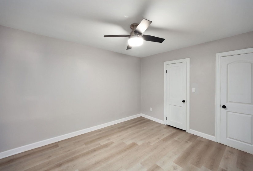 Interior space featuring neutral wall paint, wood-finish flooring, white baseboards, and two white panel doors with black hardware
