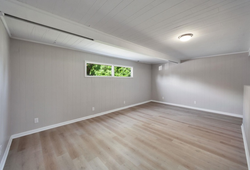 Spacious interior room featuring wood-finish flooring, light gray vertical wall paneling, and a white plank ceiling