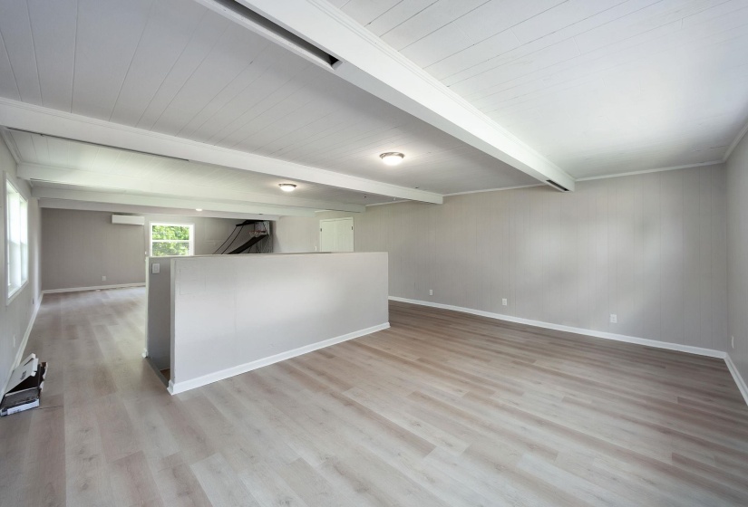 Expansive interior space featuring light wood-finish flooring, white paneled ceilings with exposed beams, and light gray wall paneling