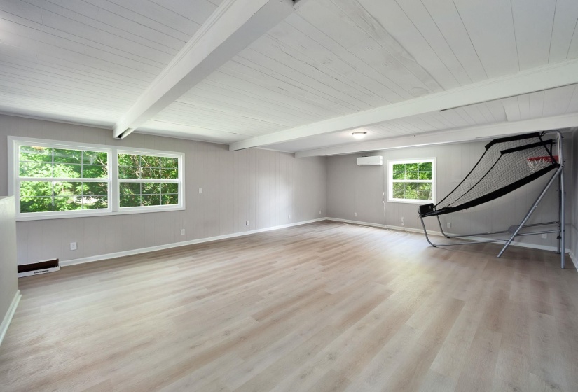 Spacious room featuring light wood-finish flooring, a white plank ceiling with exposed beams, and multiple windows