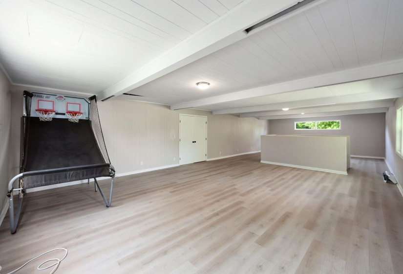 Spacious open room featuring wood-finish flooring, exposed beam ceiling, a half-wall partition, and a high horizontal window