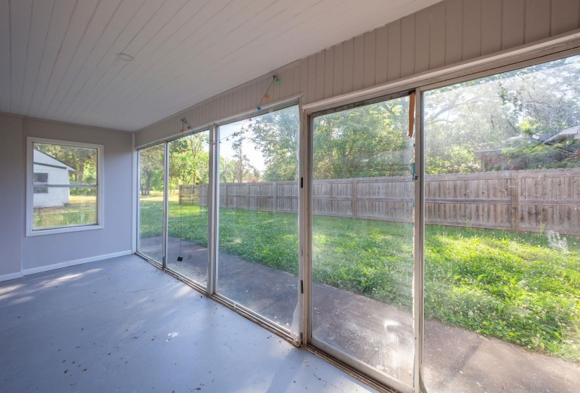 Enclosed sunroom featuring multiple floor-to-ceiling glass sliding doors, a single-pane window, and a painted wood plank ceiling