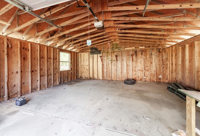 Spacious garage interior featuring exposed wood framing, wood paneling, a concrete floor, and a single window for natural light