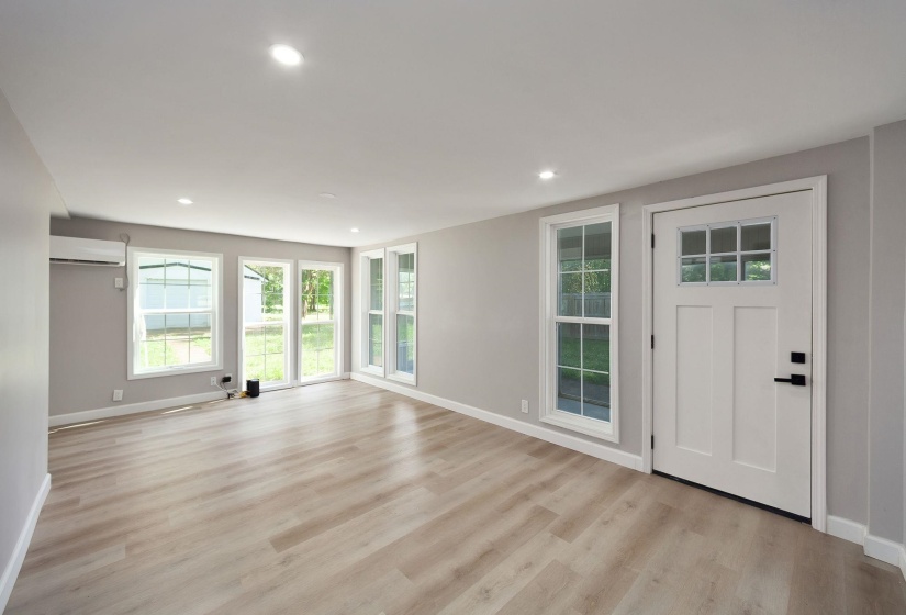 Spacious room featuring light wood-finish flooring, recessed lighting, and a modern white entry door with frosted glass