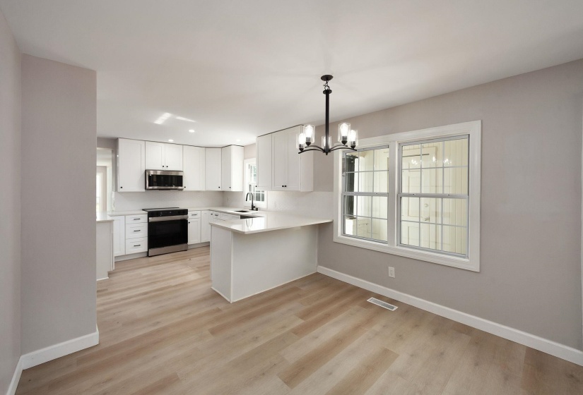 Kitchen and dining area featuring white cabinetry, stainless steel appliances, light-toned wood-finish flooring, a kitchen island with counter seating, and an overhead chandelier