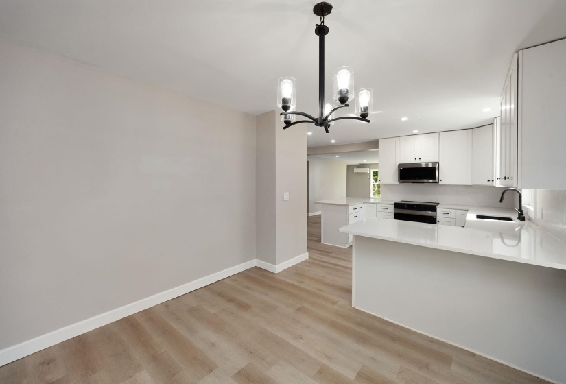 Open-concept dining area featuring a modern chandelier, wood-finish flooring, and a kitchen with white cabinetry, quartz countertops, and stainless steel appliances